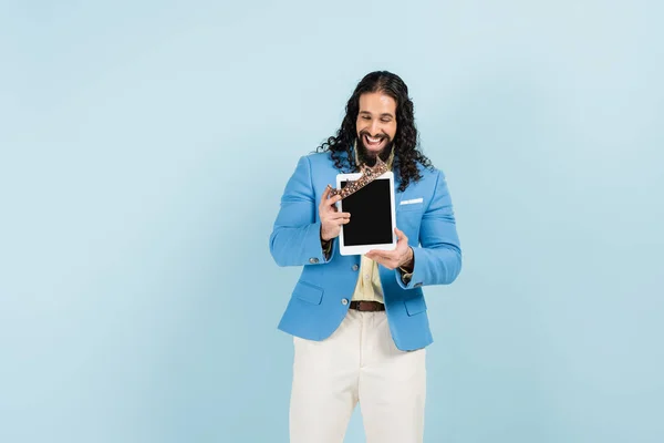 Homem hispânico feliz em casaco segurando tablet digital com tela em branco e coroa isolada em azul — Fotografia de Stock