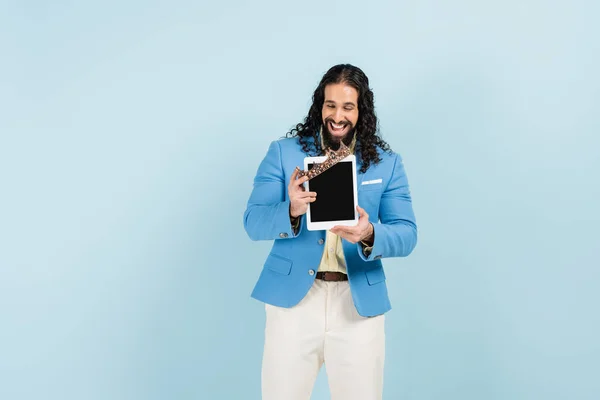 Hombre hispano feliz con chaqueta sosteniendo tableta digital con pantalla en blanco y corona aislada en azul — Stock Photo