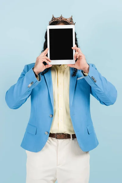 Man in jacket and crown covering face while holding digital tablet with blank screen isolated on blue — Stock Photo