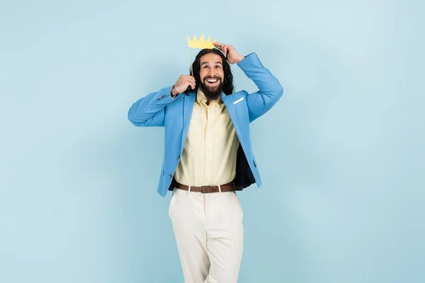 Hombre hispano feliz en chaqueta sosteniendo la corona de papel en palo aislado en azul — Stock Photo