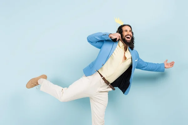 Homem hispânico feliz na jaqueta segurando coroa de papel no pau e gesticulando no azul — Fotografia de Stock