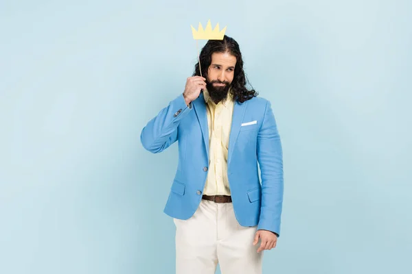 Triste hombre hispano en chaqueta sosteniendo la corona de papel en palo aislado en azul — Stock Photo