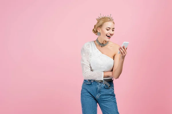Mujer alegre en la corona de lujo sosteniendo teléfono inteligente aislado en rosa — Stock Photo