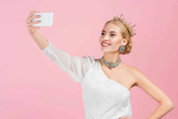 Mujer rubia en corona de lujo tomando selfie en el teléfono inteligente aislado en rosa — Stock Photo