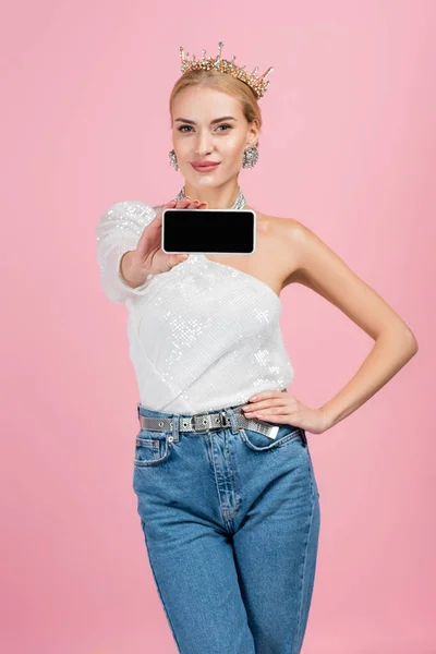 Happy blonde woman in crown holding smartphone with blank screen isolated on pink — Stock Photo