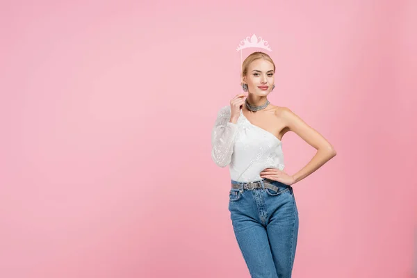 Mujer elegante sosteniendo la corona de papel en palo y de pie con la mano en la cadera aislado en rosa — Stock Photo
