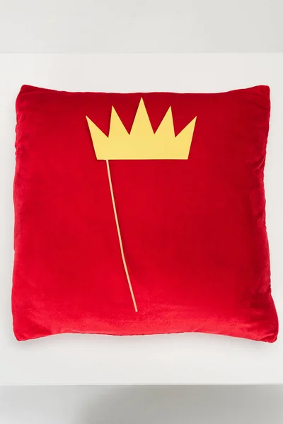 Вид зверху паперової корони на паличці і червона оксамитова подушка на сірому — стокове фото