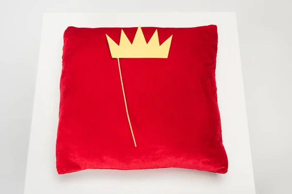 Vista superior da coroa de papel amarelo na vara e travesseiro de veludo vermelho no cinza — Fotografia de Stock