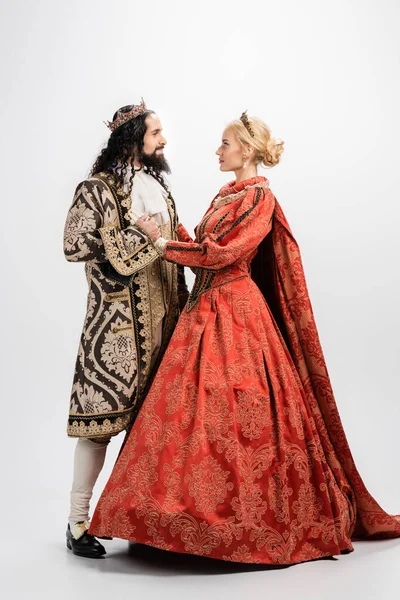 Full length of historical interracial couple in crowns and medieval clothing looking at each other on white — Stock Photo