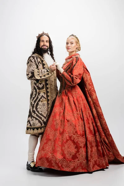 Full length of historical interracial couple in royal crowns and medieval clothing on white — Stock Photo