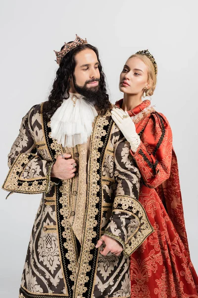 Reina rubia en corona real abrazando al rey hispano con ropa medieval aislada en blanco - foto de stock