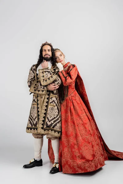 Full length of queen in royal crown leaning on hispanic king in medieval clothing on grey — Stock Photo