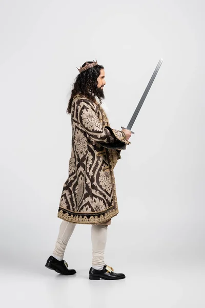 Vista lateral del rey hispano en ropa medieval y corona sosteniendo espada sobre blanco - foto de stock