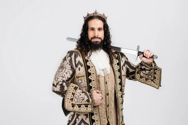 Strong hispanic king in golden crown and medieval clothing holding sword while looking at camera isolated on white — Stock Photo