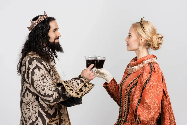 Interracial couple historique en vêtements médiévaux et couronnes cliquetis verres de vin rouge isolé sur blanc — Photo de stock