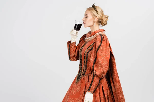 Queen in dress and crown holding glass and drinking red wine on white — Stock Photo