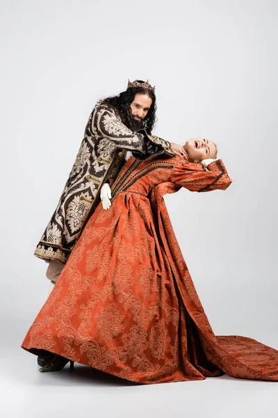 Pleine longueur de roi hispanique cruel en vêtements médiévaux étouffant reine choquée en couronne d'or sur blanc — Photo de stock