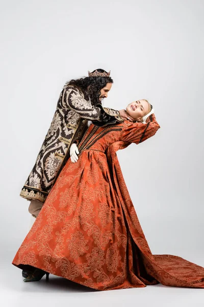 Full length of cruel hispanic king in medieval clothing choking blonde queen in golden crown on white — Stock Photo
