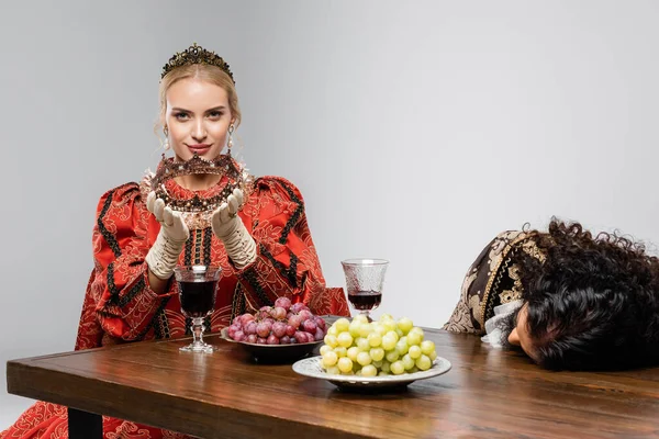 Blonde queen looking at poisoned hispanic king in medieval clothing choking isolated on white — Stock Photo