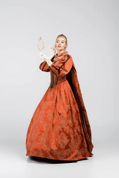 Comprimento total da rainha loira no vestido e coroa olhando para o espelho no branco — Fotografia de Stock
