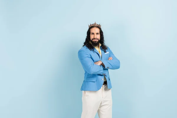 Hombre hispano barbudo en corona y chaqueta de pie con los brazos cruzados en azul — Stock Photo