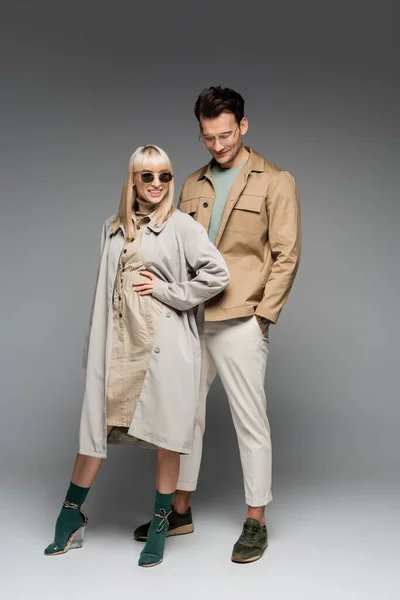 Toute la longueur de sourire couple branché posant sur gris — Photo de stock