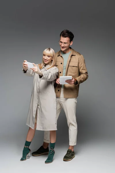 Full length of trendy models posing while taking selfie on grey — Stock Photo