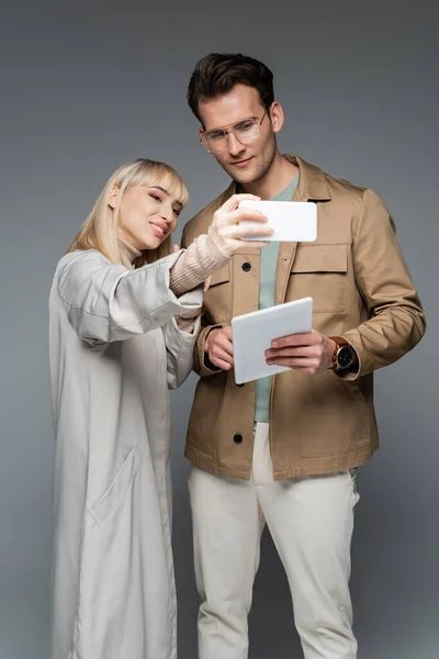 Modelos sonrientes posando mientras toma selfie aislado en gris - foto de stock