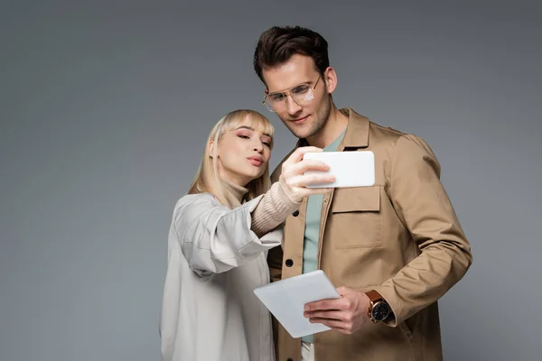 Modelli alla moda in posa mentre prende selfie isolato sul grigio — Foto stock