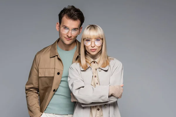 Couple élégant dans des lunettes posant et regardant la caméra isolée sur gris — Photo de stock