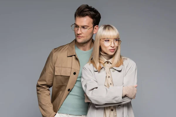 Elegante pareja en gafas posando y mirando hacia otro lado aislado en gris - foto de stock