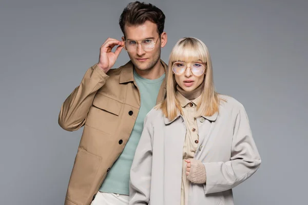 Couple à la mode dans des lunettes posant et regardant la caméra isolée sur gris — Photo de stock