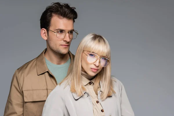 Modelo joven con estilo en gafas mirando a la cámara cerca del hombre aislado en gris - foto de stock