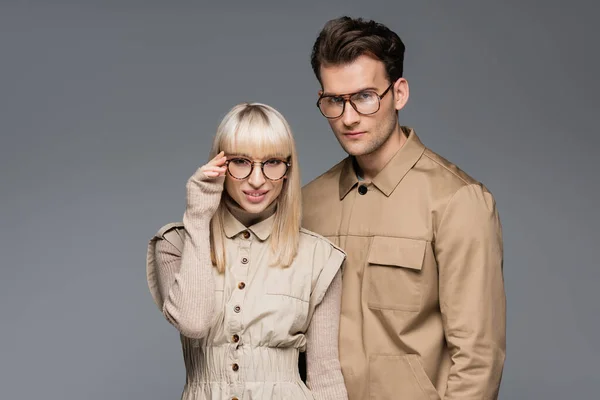 Modelo elegante ajuste de gafas y posando con el hombre aislado en gris - foto de stock