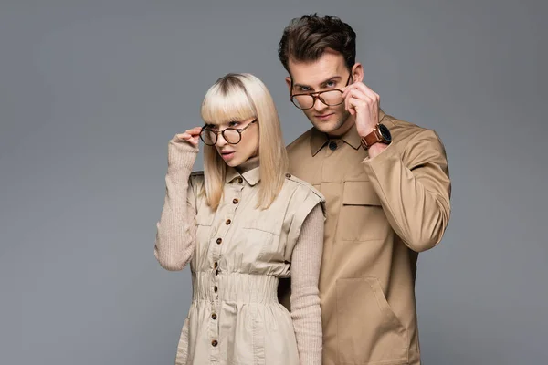 Modelos elegantes ajustando gafas y posando aislados en gris - foto de stock