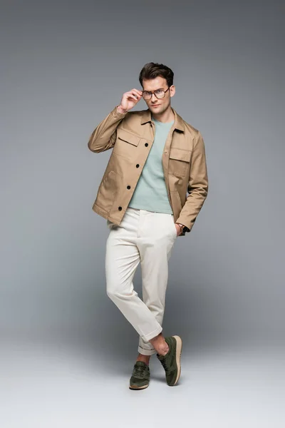 Volle Länge des trendigen Mannes in stilvollem Outfit posiert mit der Hand in der Tasche auf grau — Stockfoto