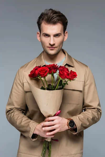 Elegante hombre sosteniendo ramo de rosas rojas aisladas en gris - foto de stock