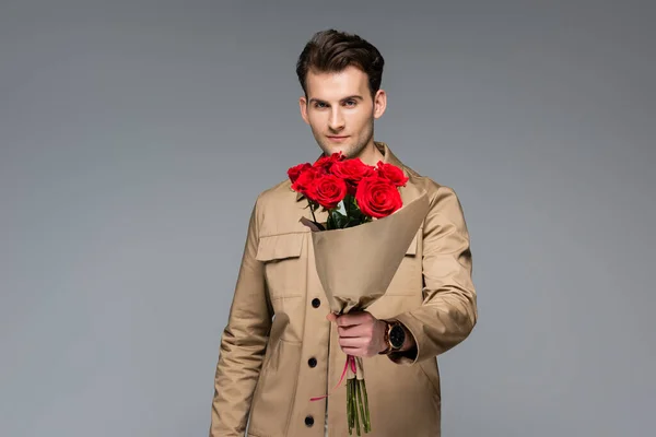 Stilvoller Mann mit einem Strauß roter Rosen auf grauem Grund — Stockfoto