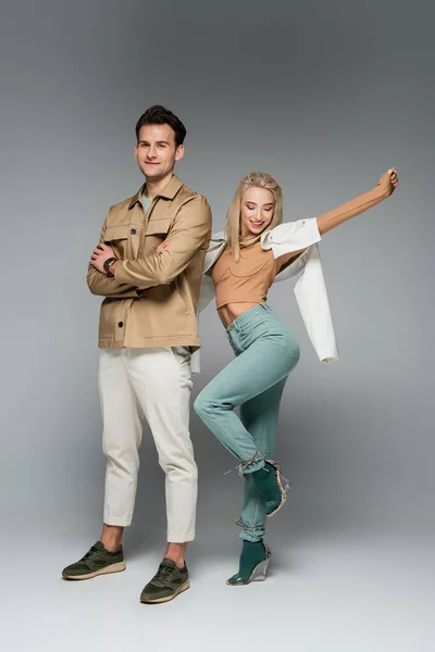 Full length of stylish models in pants and jackets posing and smiling on grey — Stock Photo