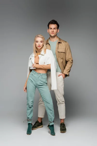 Full length of stylish model in pants and jacket posing with woman on grey — Stock Photo