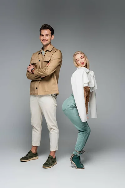 Full length of happy models in pants and jackets posing and smiling on grey — Stock Photo