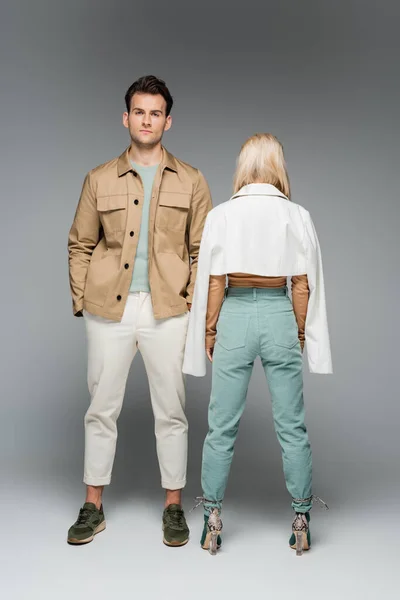 Back view of stylish woman in pants and jacket standing near model on grey — Stock Photo