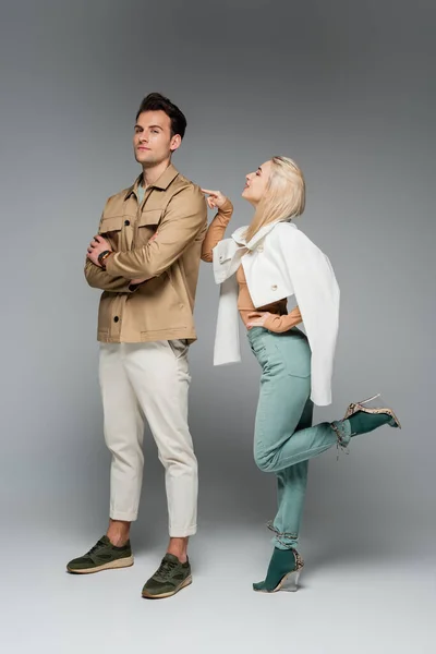 Stilvolles Modell in Hose und Jacke, das auf einen Mann zeigt, der auf grau posiert — Stockfoto