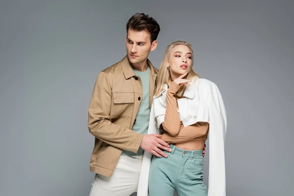 Elegante pareja en pantalones y chaquetas posando aislados en gris - foto de stock