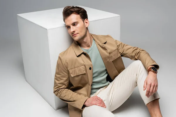 Trendy man posing while leaning on white cube on grey — Stock Photo