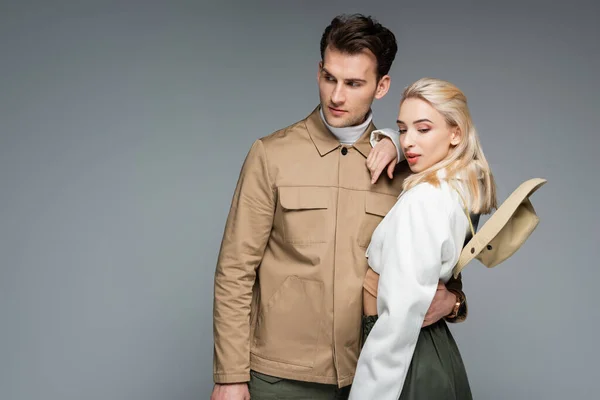 Stylish man in jacket hugging blonde woman isolated on grey — Stock Photo