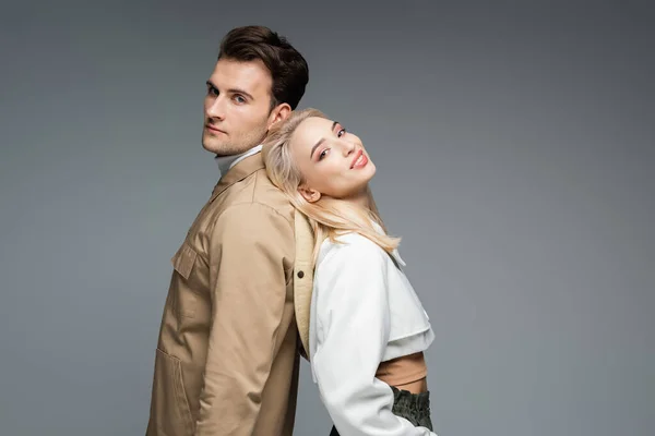 Man in jacket standing back to back with cheerful blonde young woman isolated on grey — Stock Photo