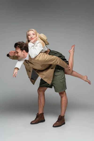 Comprimento total de homem feliz piggybacking mulher alegre no cinza — Fotografia de Stock