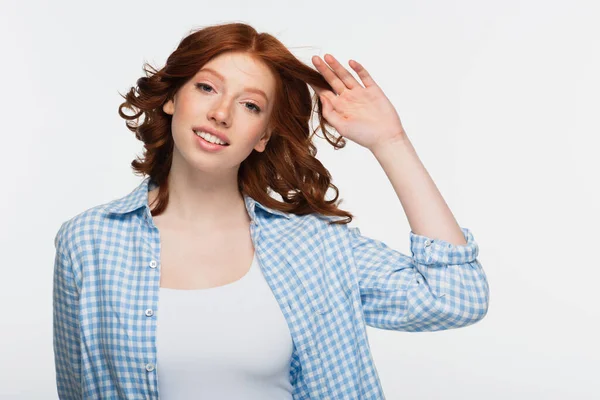Молода жінка в синій картатій сорочці, що регулює червоне волосся, ізольована на білому — стокове фото