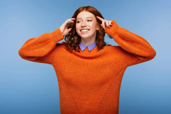 Fröhliche rothaarige Frau in orangefarbenem Pullover, die vereinzelt auf blauem Grund wegschaut — Stockfoto